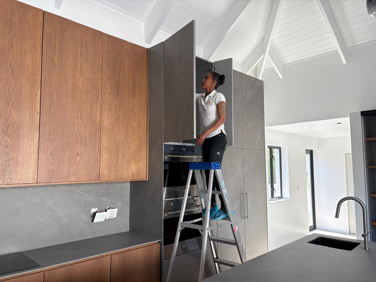 Cleaner on a ladder finishing post-construction cleaning in a modern kitchen
